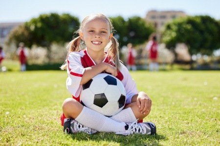 Child smiling while holding soccer ball on field